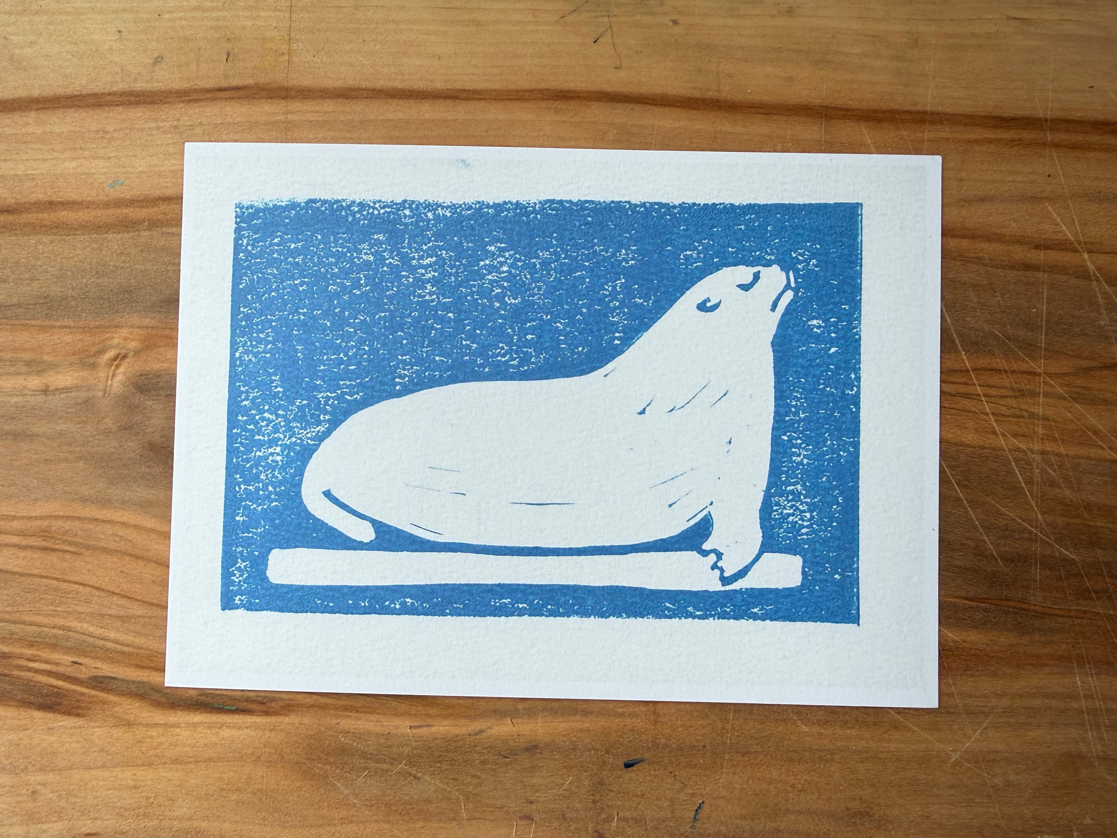 Print of a seal on blue background with white border, placed on a wooden surface.